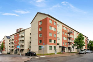 Flerbostadshus i puts och tegel längs lokalgata med parkerad mörk bil