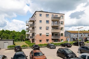 Flerfamiljshus med tegelfasad, balkonger omgiven av grönska och parkeringar framför huset under klar himmel