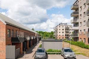 Flerfamiljshus med tegelfasad, balkonger med grönska och parkeringar mellan bostadshusen