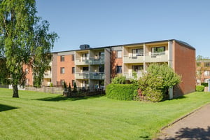 Flerbostadshus i tre våningar med gräsmatta och grönska utanför