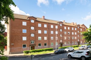 Flerbostadshus i rött tegel med parkeringar och gräsmatta framför
