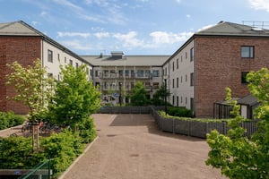 Bostadshus i ljus fasad med flera våningar med balkonger, som omger innergård med grönområde under en molnig himmel