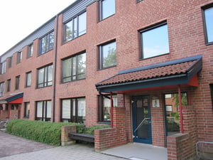 Flerfamiljshus i rött tegel med flera våningar, stora fönster och en entrédörr med tak