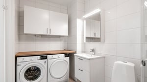 Tvättstuga i ljusa toner med tvättmaskin, torktumlare, kommod, spegel och väggskåp