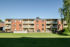 Flerbostadshus i tre våningar med balkonger och uteplatser, med gräsmatta och grönska utanför