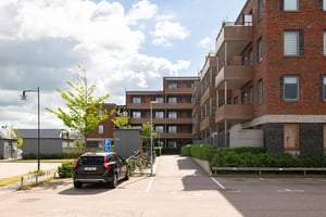 Flerfamiljshus med tegel- och putsfasad, balkonger och parkeringar framför byggnaden
