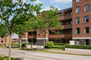 Flerfamiljshus med tegel- och putsfasad, balkonger och grönska framför byggnaden