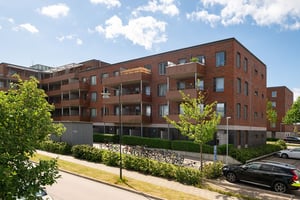 Flerfamiljshus med tegel- och putsfasad, balkonger och parkeringar på sidan om byggnaden