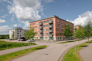 Flerbostadshus i rött med parkeringar och gräsmatta framför