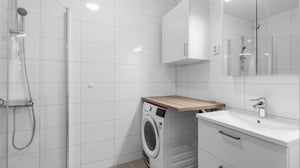 Modernt badrum med dusch, tvättmaskin, handfat och ljusa kakelväggar