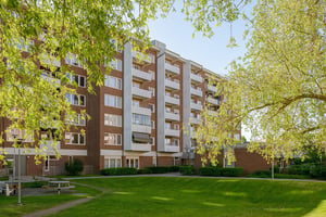 Bostadshus i brun fasad med flera våningar med balkonger, omgiven av grönska på innergård under en klar himmel
