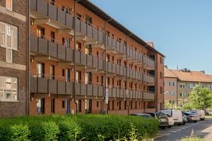 Flerbostadshus i rött tegel med bruna balkonger, med lokalgata framför huset