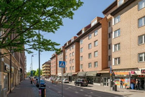 Flerfamiljshus med tegelfasad med lokaler i bottenplan, omgiven av gator under klar himmel