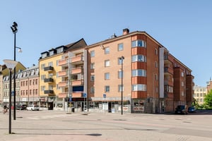 Flerfamiljshus med tegelfasad, balkonger omgiven av gator och torg under klar himmel