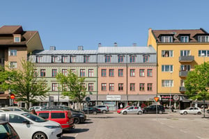 Flerfamiljshus i grönt, rosa och gult i olika antal våningar, omgiven av gator och torg under klar himmel