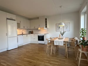 Kök med vit inredning och vitvaror, samt matplats möblerad med bord och fyra stolar i ljust träslag.