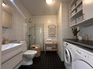 Badrum med vitt kakel och grått klinker på golvet, utrustat med tvättmaskin, torktumlare och duschväggar i glas.