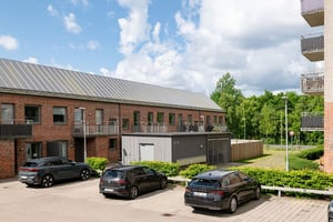 Flerfamiljshus med tegelfasad, balkonger och parkering med tre svarta parkerade bilar mellan fastigheterna