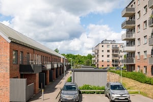 Flerfamiljshus med tegelfasad, balkonger med grönska och parkeringar mellan bostadshusen