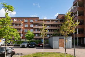 Bostadshus i tegel med flera våningar med balkonger, parkering och grönområde under en molnig himmel
