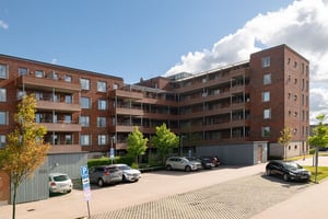 Bostadshus i tegel med flera våningar med balkonger, parkering och grönområde under en molnig himmel