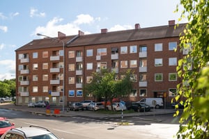 Flerbostadshus i rött tegel med vita balkonger, med parkerade bilar utanför längs gata