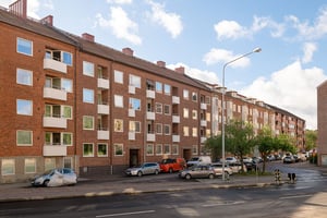 Flerbostadshus i rött tegel med vita balkonger, med parkerade bilar utanför längs gata