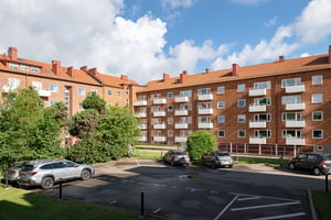 Flerbostadshus i rött tegel med vita balkonger, med bilar parkerade på p-platser vid innergård