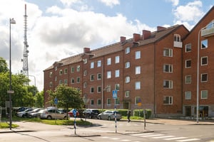 Flerbostadshus i rött tegel  med parkeringar och träd framför