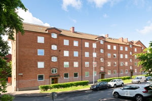 Flerbostadshus i rött tegel  med parkeringar och gräsmatta framför