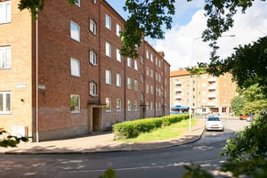 Flerbostadshus i rött tegel  med parkeringar och träd framför