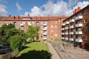Flerbostadshus i rött tegel med vita balkonger mot grön innergård med gräsmatta och träd