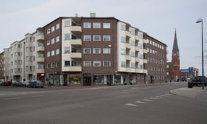 Flerbostadshus vid en gata med butikslokaler på markplan och kyrka i bakgrunden