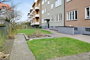 Bostadshus med flera våningar, omgivna av en trädgård med gräsytor, stengångar och rabatter
