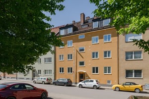Gul flerfamiljsbyggnad med flera våningar, personbilar parkerade framför