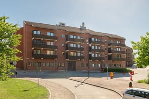 Flerbostadshus i rött tegel med bruna balkonger, med lokalgata framför huset