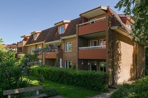 Flerfamiljshus med tegelfasad, balkonger omgiven av grönska under klar himmel