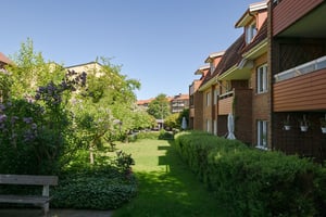 Flerfamiljshus med tegelfasad, balkonger omgiven av grönska under klar himmel