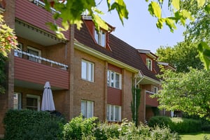 Flerfamiljshus med tegelfasad, balkonger omgiven av grönska under klar himmel
