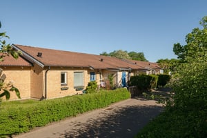 Flerbostadshus i tegel, i radshuslänga med grön häck mot gata