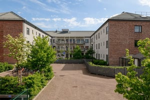 Bostadshus i ljus fasad med flera våningar med balkonger, som omger innergård med grönområde under en molnig himmel