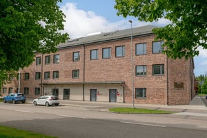 Bostadshus i tegelfasad med flera våningar, omgiven av parkering och lokalgata molnig himmel
