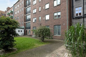 Flerfamiljshus i tegel med stora fönster och grönskande träd på innergård