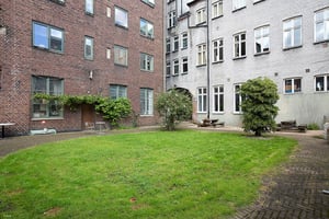 Flerfamiljshus i tegel med stora fönster och grönskande träd på innergård