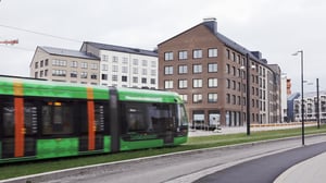 Grön spårvagn passerar framför moderna flerfamiljshus i stadsmiljö