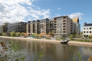 Flerbostadshus i ljus fasad med balkonger mot parkliknande promenadstråk längs vattenkanal