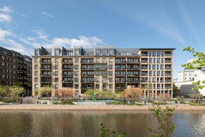 Flerbostadshus i ljus fasad med balkonger mot parkliknande promenadstråk längs vattenkanal
