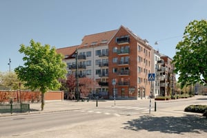 Nybyggnad med flerfamiljshus i tegel och ljusa fasader, omgiven av grönska och en gata i förgrunden