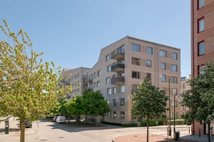 Flerfamiljshus i ljust tegel med balkonger omgivet av grönska och en gata med parkeringar