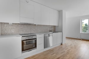 Modernt kök i inflyttningsklar lägenhet med vita skåp, integrerad diskmaskin och ljus öppen planlösning